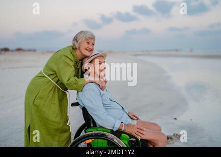 Senior man on wheelchair enjoying together time with his wife at sea. Stock Photo