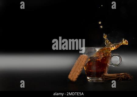 Splash in glass cup of black tea isolated on black background with delicious cookies, copy space detox healthy medicine Stock Photo