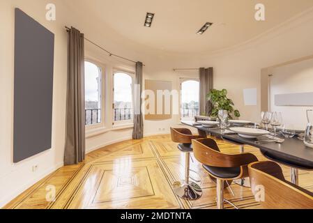 Semicircular living room with varnished hardwood floors with a high gray board table and wooden and chrome metal stools Stock Photo