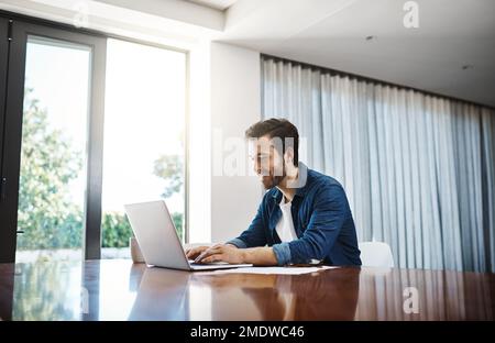 ive got all the space I need to work here at home. a handsome young businessman sitting down and using his laptop while working from home. Stock Photo