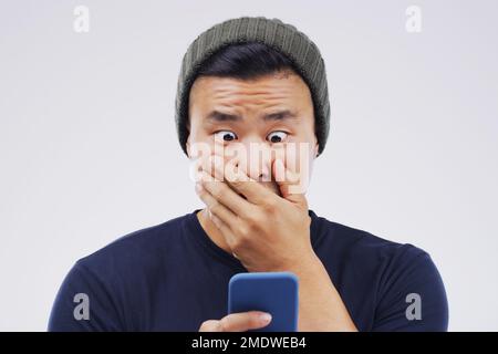 Looks like Ive been catfished. Studio shot of a young man looking surprised while using his cellphone. Stock Photo