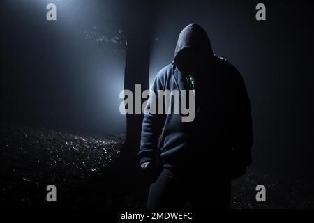 Hooded man in the dark forest at backlight Stock Photo