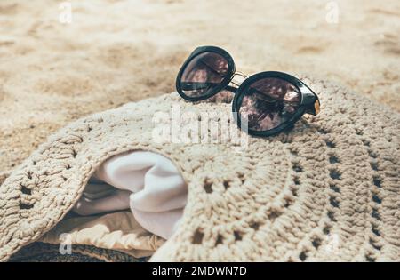 Exotic beaches still life: knitted shoulder bag with fashionable black sunglasses lying on the sand under the palm trees. Summer vacations concept ima Stock Photo