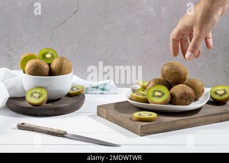 Hand taking a fresh kiwi from a white plate on white wood base. Stock Photo