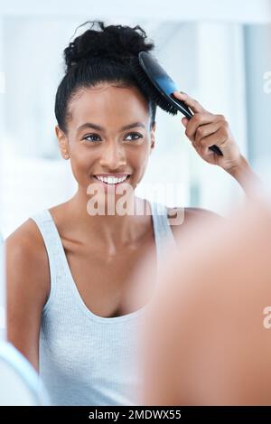 Everything is good when its a good hair day. a beautiful young woman brushing her hair in the bathroom at home. Stock Photo