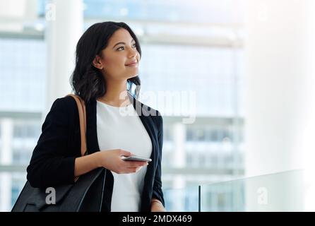 Shes got smart ideas for the day ahead. an attractive young businesswoman looking thoughtful while holding a smartphone in a modern office. Stock Photo