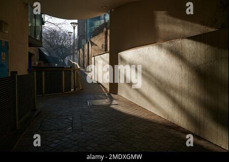 22 Jan 2023 - LondonUK: Walkway though covered walkway through built up estate in low winter sun Stock Photo