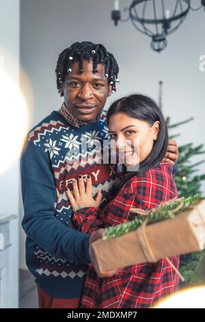 Diverse young couple hugging with presents near the Christmas tree. High quality photo Stock Photo