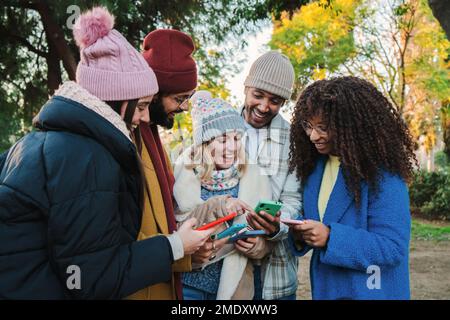 Portrait of a group of multiracial young fiends watching videos on a social media app using an cellphone with autumn clothes. Multiethnic people having fun using their smartphones. Communication concept. High quality photo Stock Photo