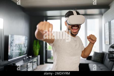 VR, angry and man boxing with glasses, training for a fight and match. Futuristic, digital sports and gamer punching while playing in an augmented Stock Photo