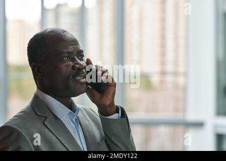 Side view of confident mature African American broker with mobile phone communicating with colleague or arranging appointment Stock Photo