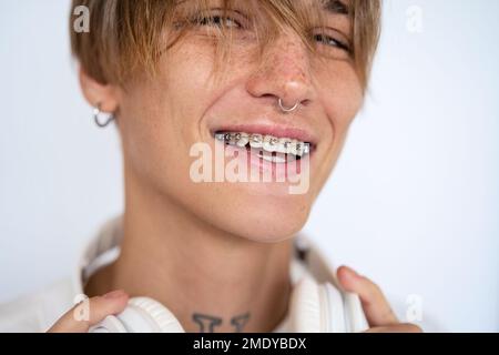 Portrait stylish blonde short haired woman with facial piercing and dental braces looking at camera and smiling against white background. Stock Photo