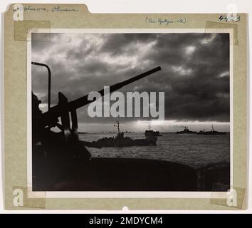 L-Day Plus One Off Okinawa. The sun goes down over the American task force off Okinawa on L-Day plus one. After a terrific fleet bombardment and the assault of Coast Guard-manned and Navy landing craft, the situation is well in hand. In foreground, an anti-aircraft gun on a Coast Guard-manned LST is alerted for possible Japanese air attacks against the invaders. Stock Photo