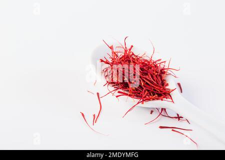 Saffron in white spoon on white background. Natural dry saffron threads from crocus flowers. Stock Photo