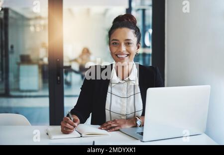 Watch me put my ambition to work. a young businesswoman making notes at her desk in a modern office. Stock Photo