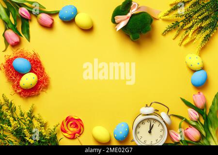 Easter frame. Eggs bunny flowers alarm clock on a yellow background. Place for text Stock Photo