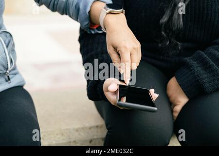 woman's hand with smart watch pointing to smart phone, holding in her hand young latina woman, front view without recognisable faces Stock Photo