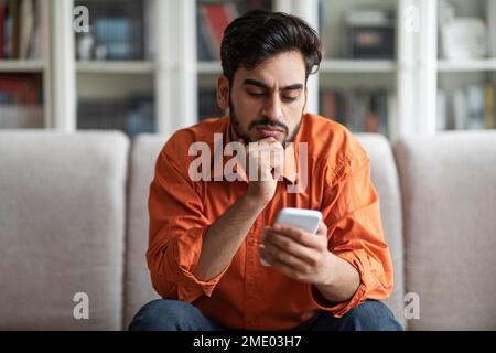 Thoughtful handsome middle eastern man using phone at home Stock Photo