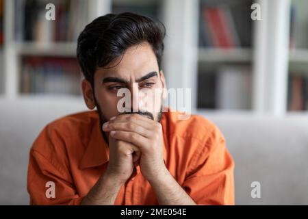 Pensive young arab man sitting on sofa at home Stock Photo