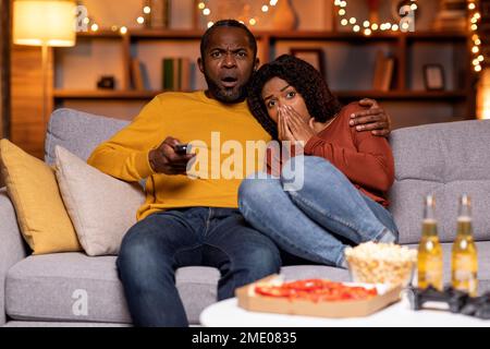 Frightend black couple watching horror movie at home Stock Photo