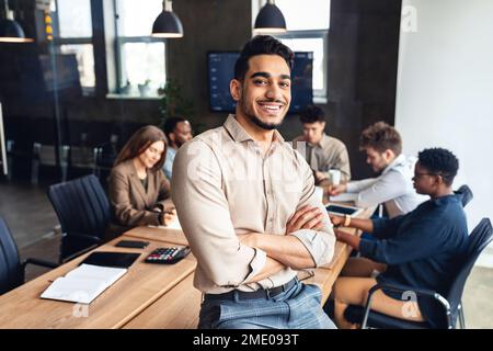 Successful person. Confident arab businessman leaning on desk in office, posing with folded arms and smiling at camera Stock Photo