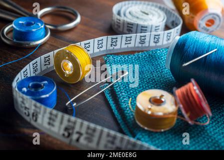 Sewing items - thimble, needle, measuring tape, spools of blue thread, including pins. Blue fabric for sewing on background. Stock Photo