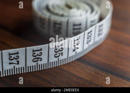 Close up tailor measuring tape on wooden table background. White measuring tape shallow depth of field. Stock Photo