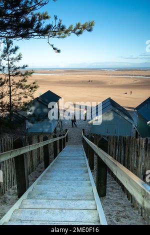 Steps between beach huts leading to beach with view accross the sand to sea at Wells on Sea North Norfolk East Anglia England Stock Photo