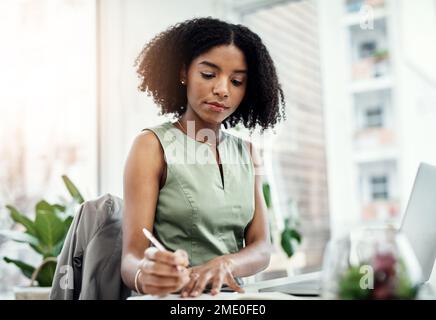 Working diligently. an attractive young businesswoman writing in her diary while working in the office. Stock Photo