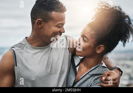 Im glad were doing this together. an affectionate and athletic young couple standing with their arms around one another outdoors. Stock Photo