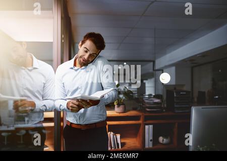 Hes a guy who gets things done quickly. a young businessman using a notebook while talking on a cellphone in an office. Stock Photo