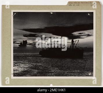 A Coast Guard-manned invasion transport is silhouetted against the sunset off Leyte Island in the Philippines, while a cloud formation resembling a giant bomber looms above. The image captures the drama of war and nature's unusual shapes during the twilight hours. Stock Photo