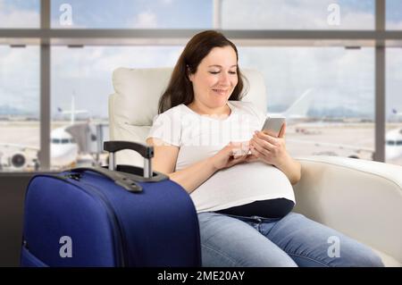 Pregnant woman texting with a smart phone and waiting for her flight in a VIP area and VIP zone aiport Stock Photo