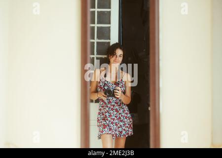 Young female in romantic dress standing against long rectangular mirror and taking photo of herself on professional camera Stock Photo