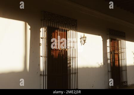 Exterior white wall of house with doors covered with metal privacy grills lit with sunlight in Cuba Stock Photo