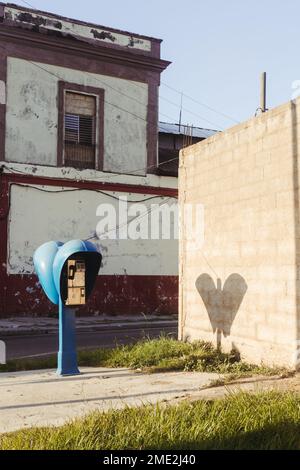 Exterior of brick wall with public pay telephone against shabby aged house in town of Cuba in sunlight Stock Photo