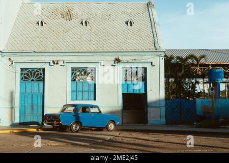 Exterior of aged house with blue colored doorways and parked blue old car parked near on sidewalk Stock Photo