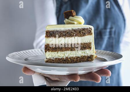 Crop unrecognizable female confectioner in apron serving delicious piece of cake with white glaze and whipped cream on ceramic plate Stock Photo