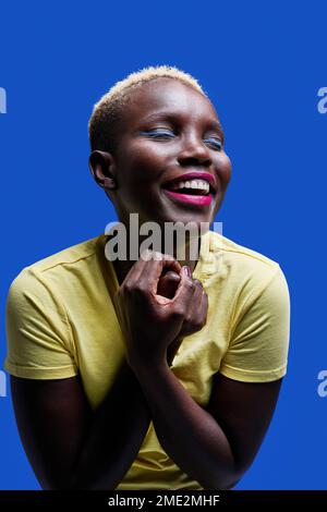 Happy young African American female in yellow t shirt smiling against blue background Stock Photo