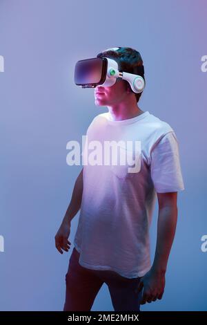 Unrecognizable male in casual t shirt standing in neon light in studio with VR goggles and exploring cyberspace Stock Photo