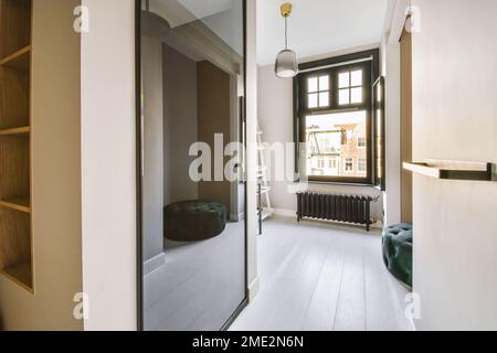 Window with wooden frame and mirror hanging on wall against wardrobe with empty shelves in contemporary apartment on sunny day Stock Photo