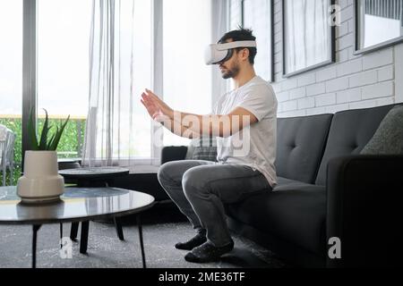 Virtual reality glasses, metaverse and man on sofa with headset for streaming interactive, online and 3d games. Futuristic tech, user interface and Stock Photo