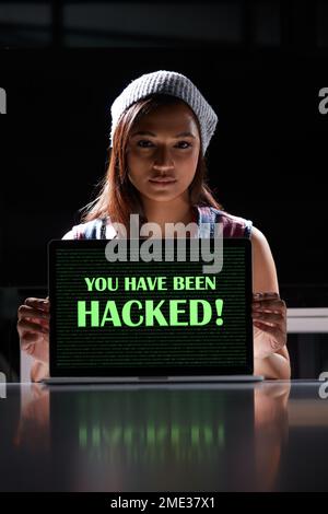 The dodgy world of cybercrime. a young female hacker using a laptop with the words You have been hacked on it. Stock Photo