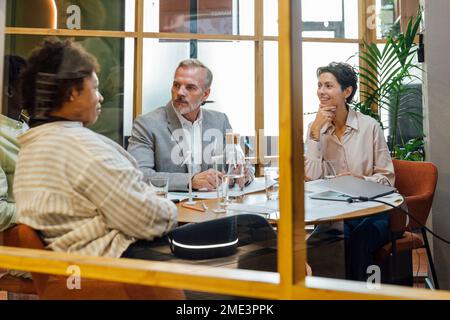 Happy businesswomen discussing with businessmen at table in office Stock Photo
