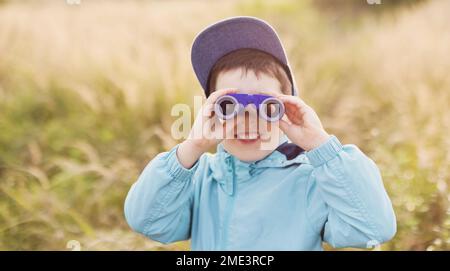 Happy boy looking through binoculars on field Stock Photo