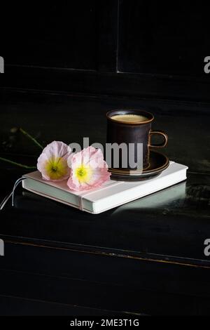 Iceland poppy flowers by coffee cup on diary over black piano Stock Photo