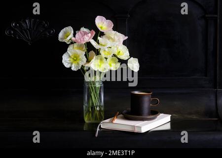 Iceland poppy flowers in glass jar by coffee cup and diary on black piano Stock Photo