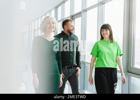 Three happy business people in green clothing walking on office floor Stock Photo