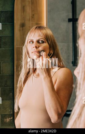 Woman applying make-up with brush in bathroom at home Stock Photo