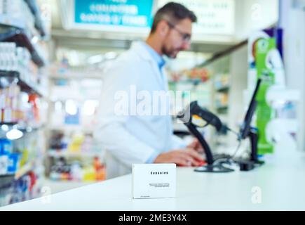 Recommended by pharmacists. a medicine package on the pharmacy counter while an unrecognizable male pharmacist works in the background. Stock Photo